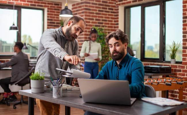 "Group of digital marketing professionals collaborating on laptops and charts, discussing social media and SEO strategies in a modern office setting.